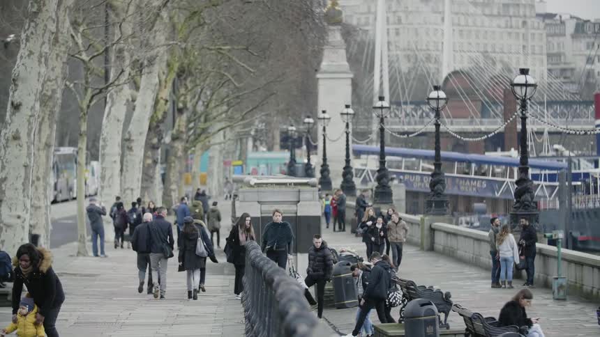 People walk and sit along the waterfront in a city