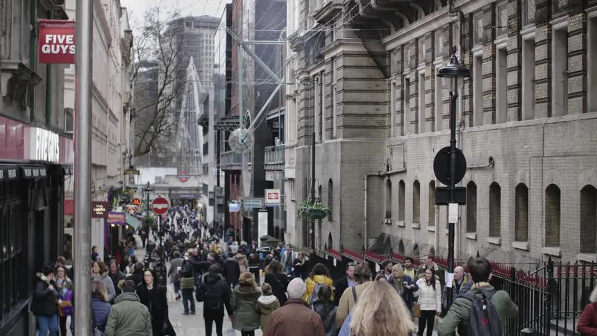A large crowd of people walk the city sidewalk