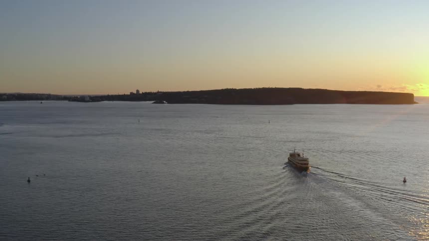 Rising sun casts light across ocean as ship travels toward city on the shore