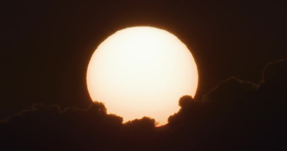 Large sun hovers over the horizon turning clouds into silhouettes