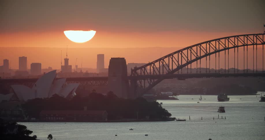 Large bright sun goes down in the sky behind the city skyline and the sydney opera house