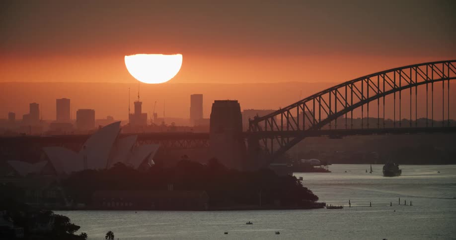 The sun setting behind the sydney opera house as boats float on the water