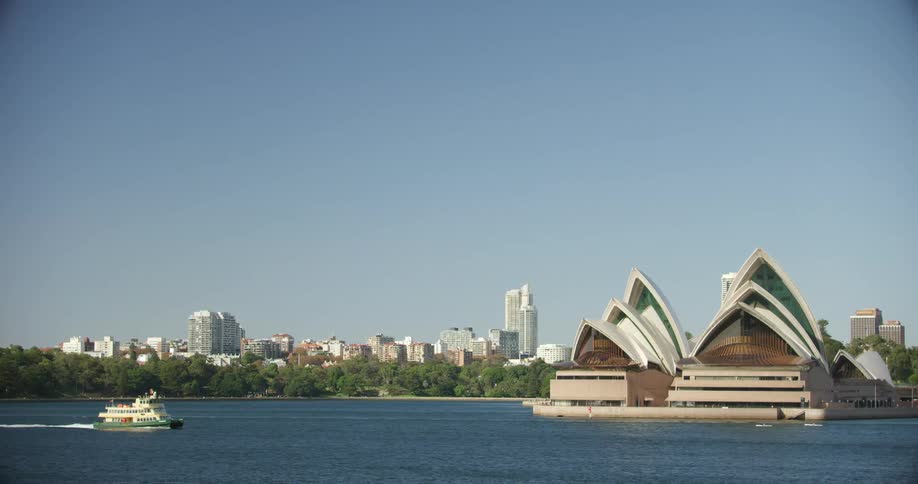 A boat on the water in front of a city skyline going towards the australia opera house