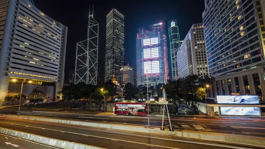 Traffic moves through a city with skyscrapers flashing neon lights