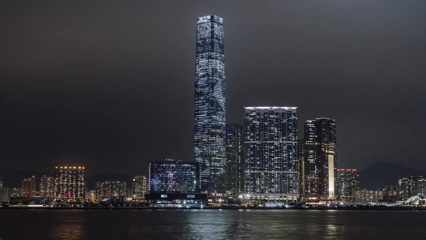 Skyscraper lights form letters and symbols as ships pass across water at night