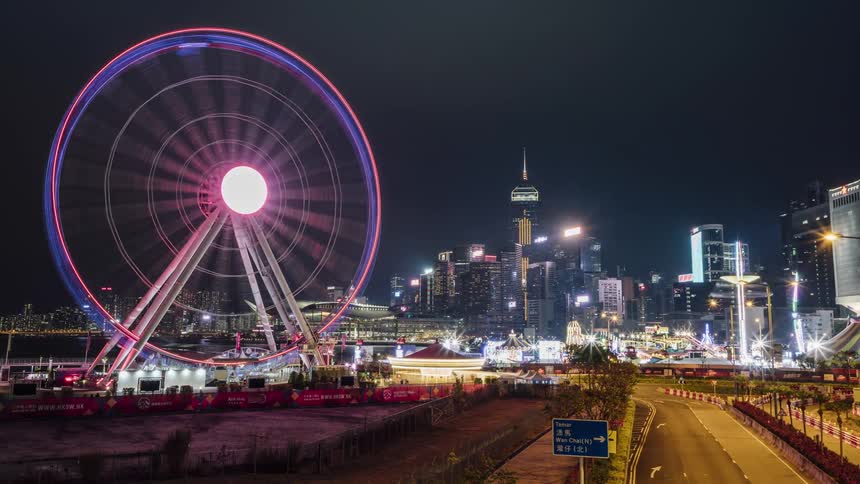 Time lapse of an amusement park and cars driving in front of a city skyline