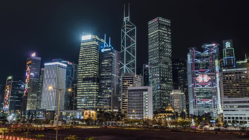 Vehicles drive buildings on the highway in front of the tall and illuminated buildings at night in the city