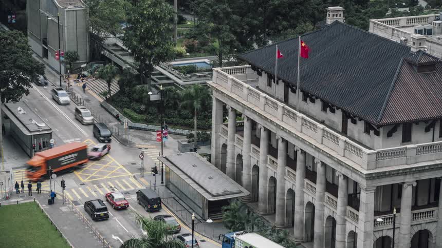 Traffic travels through intersection near buildings and heavily treed area