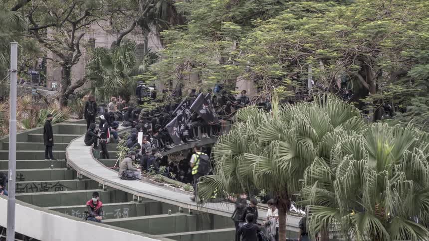 Crowd of people dress in masks and dark clothes waving flags at even near outdoor steps