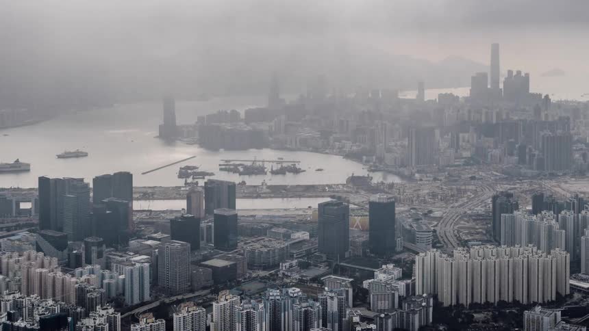 Fog and clouds pass over a city as cars travel on city streets and boats move through the harbor