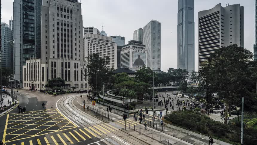 A large crowd of people moving throughout a park and intersection in a metropolis