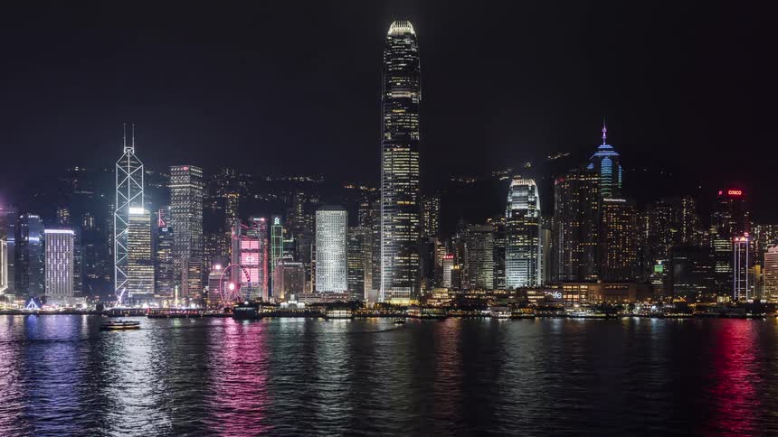 Boats cross water reflecting city lights at night