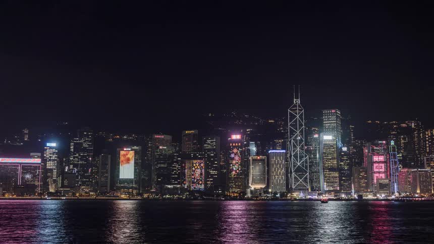 Boats speed past a city skyline lit up at night