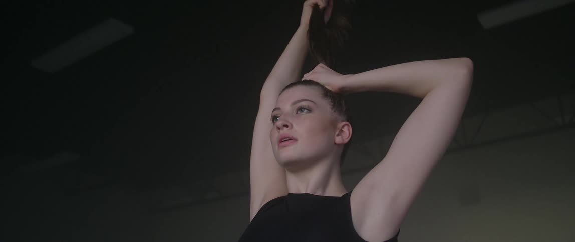 A woman pulls her hair straight up then releases it as part of a dance