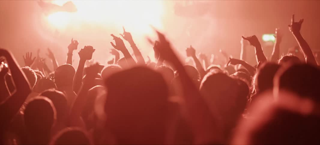 People in a concert with their hands up and lights flashing