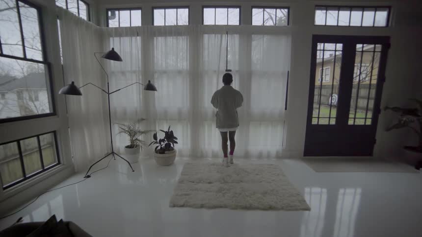 Woman walking over to window pulling curtain back then looking out