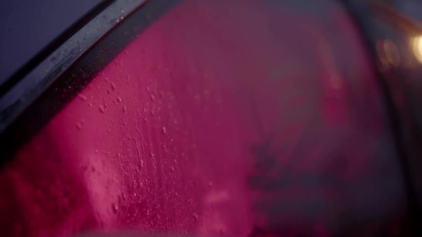 Rain falls on a rolled up car window with a person barely visible behind the glass