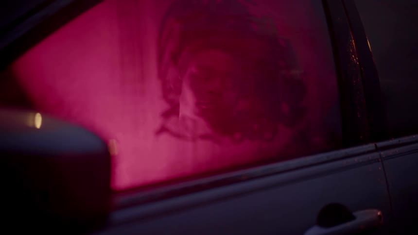 A person sits in a car looking out the steam covered window with a hand wiped clearing on a rainy night