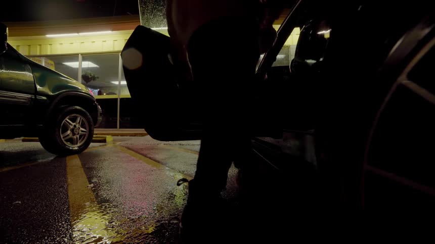 Man walks out of store and into a car at night while raining