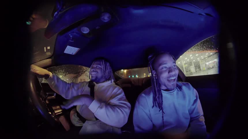 Two men laugh and talk in a car as one man drives