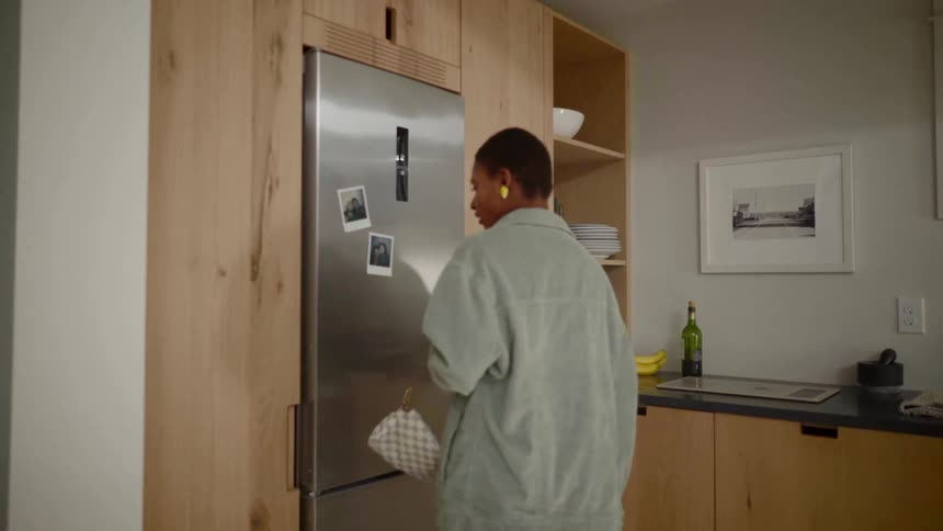 Black woman at the kitchen and looking at pictures attached to her refrigerator