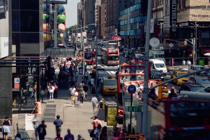 Pedestrians walk down the busy street while the vehicles drive on the highway