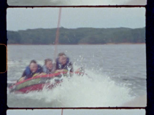 Three kids hold on and laugh as they ride a tube being pulled by a boat