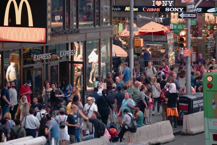 Scores of people walk up and down a city sidewalk