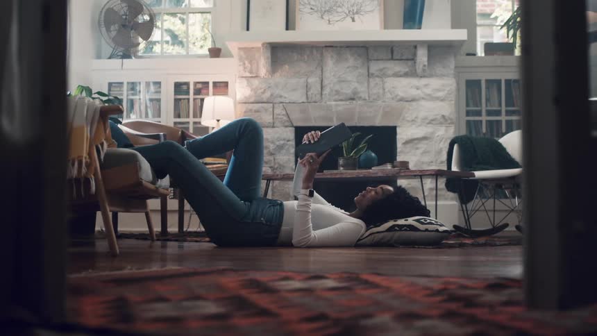A teenager lies on the floor and talks with someone on her tablet