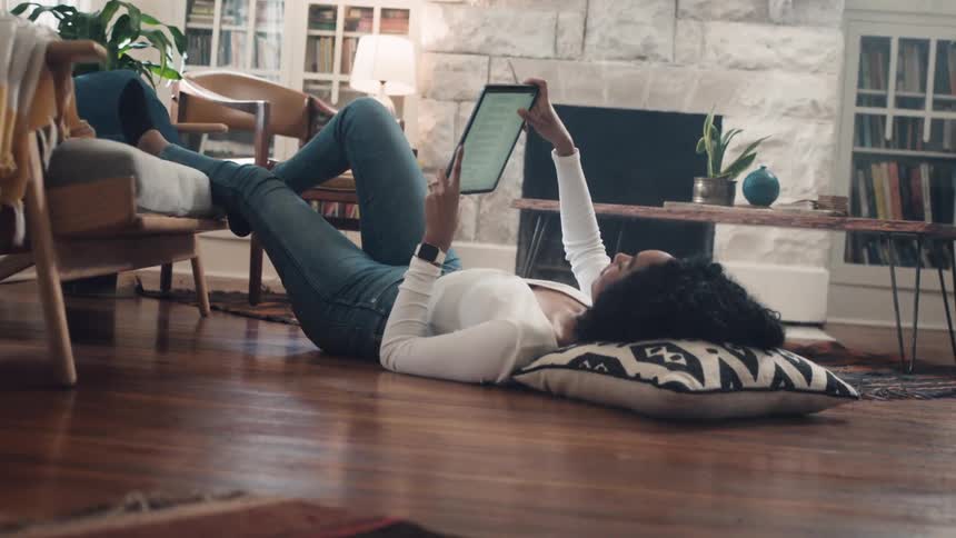 Woman reclines on floor reading on tablet near fireplace