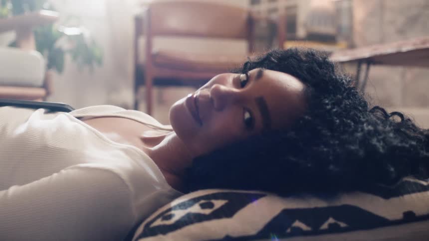 Black woman lying down on the floor looks at the camera in the living room at home
