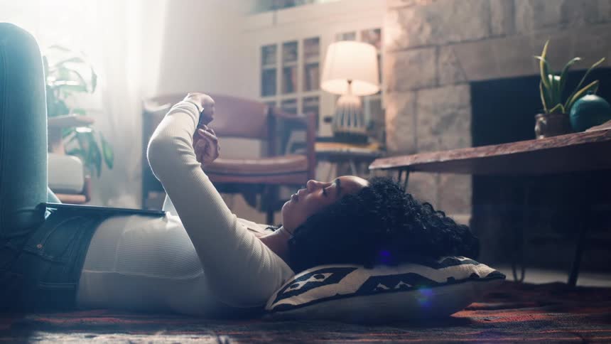 A teenager lying on the floor puts her tablet on her stomach and scrolls through her watch
