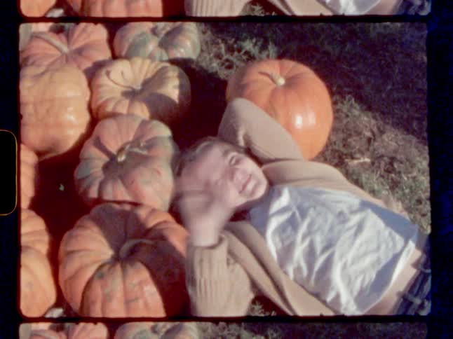 Girl lying on ground among pumpkin pile smiles and waves