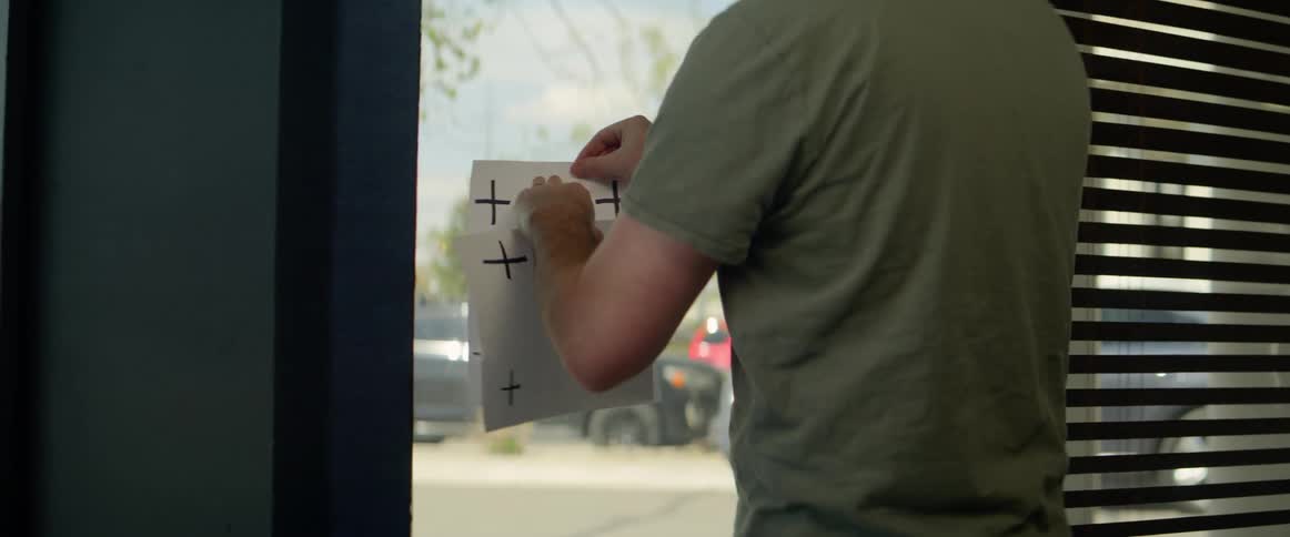 A man takes off a paper sign and places another one just like it on a glass window door