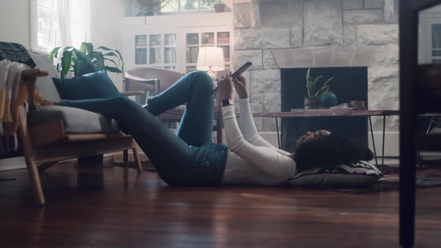 A woman laying on the floor on a pillow while using a tablet