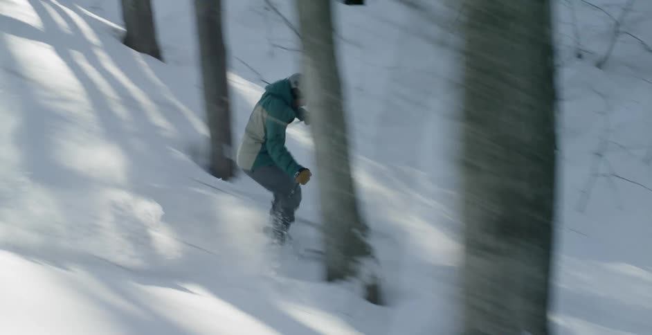A skier moves quickly down a bumpy slope with several trees