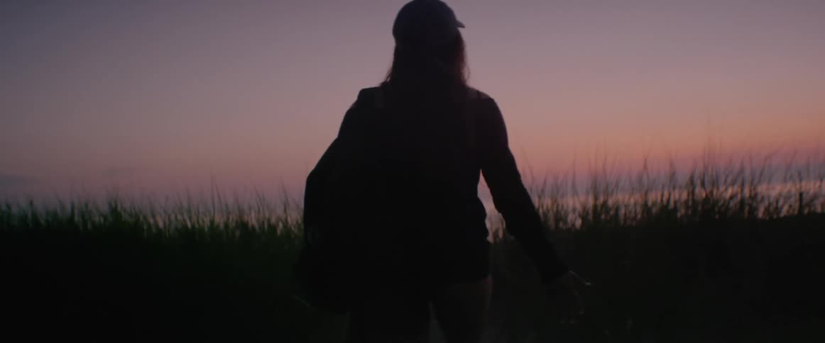 A white woman walks along a path to a beach