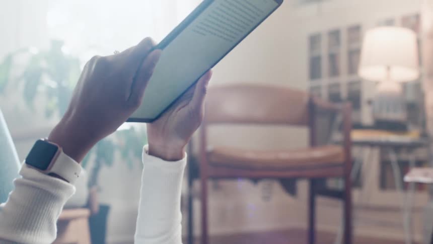 A black woman lies on the floor while reading text on a tablet