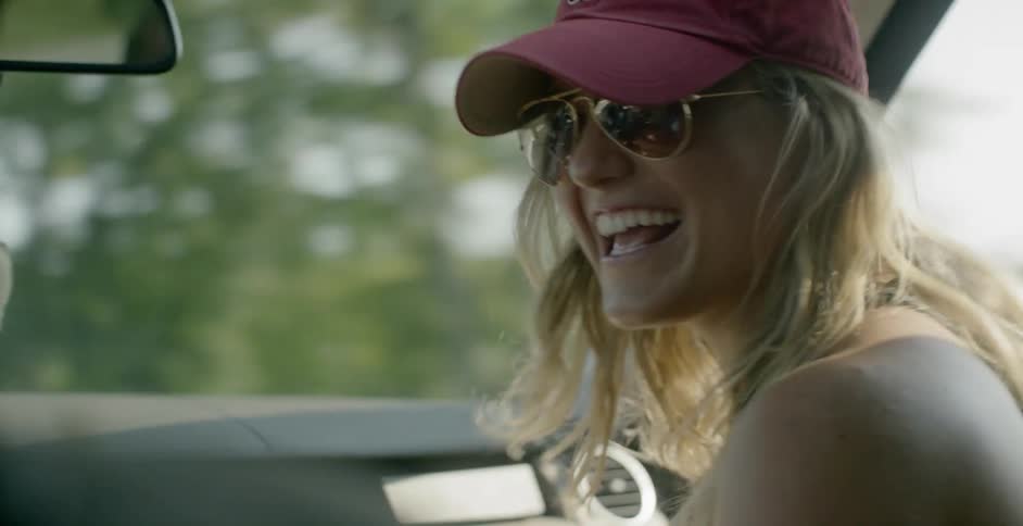 Woman wearing sunglasses and hat talks to driver inside car