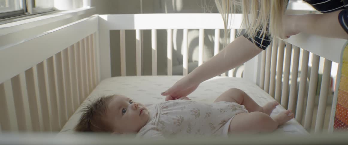 A mother leans over a crib and touches her daughter