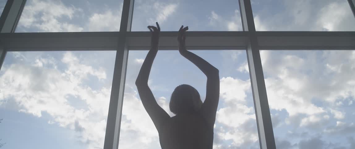 A woman is waving her arms around in front of a large window