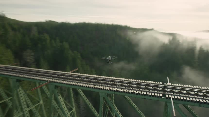 A drone hovers over a train trestle connecting two mountains