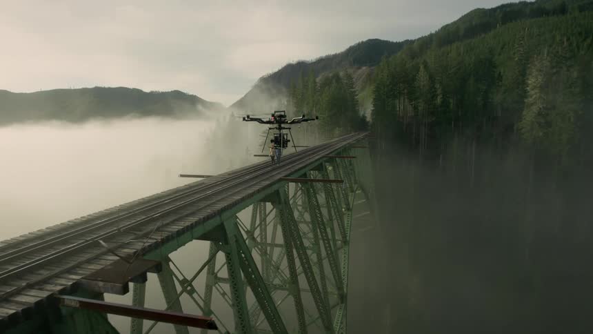 A drone hovers near a couple as they walk across train trestle
