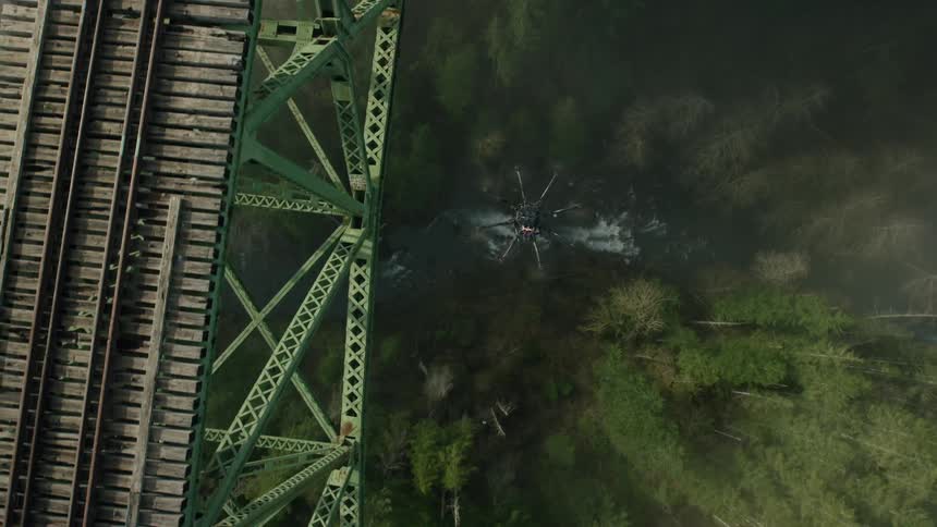 A drone flies beside a railway bridge above a valley