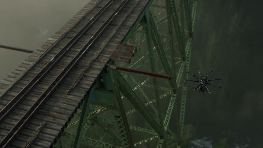 A drone flies near a couple crossing a train bridge