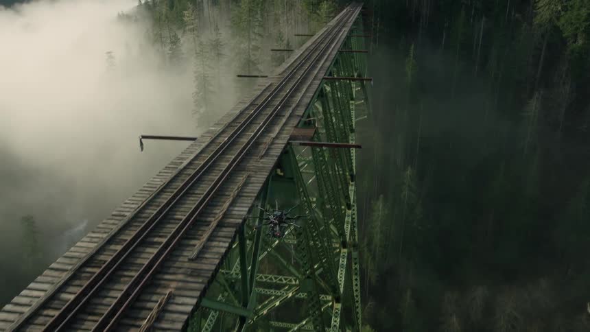 A drone flies high over a bridge with train tracks on it