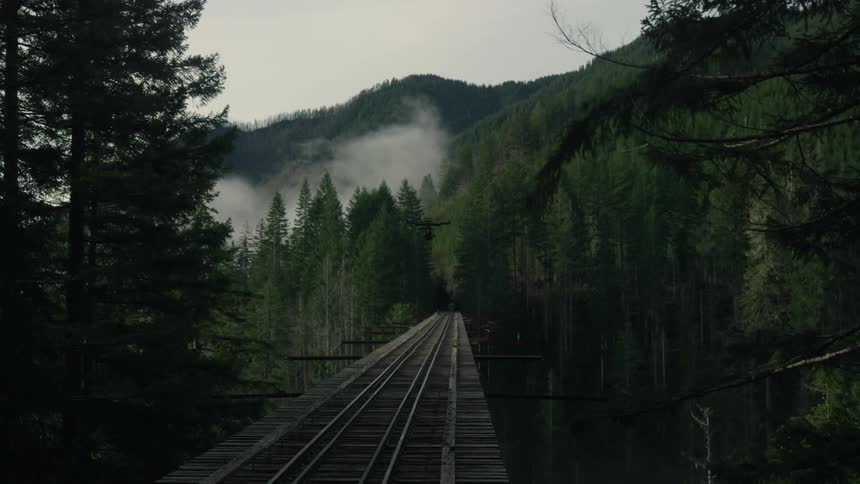 A drone flies over a trestle bridge in a mountain forest