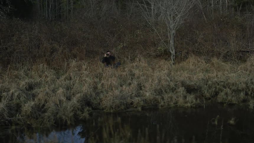 A person is crouched by the water taking pictures