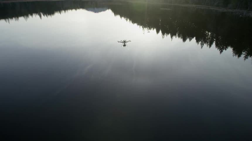 A drone flies over a smooth lake