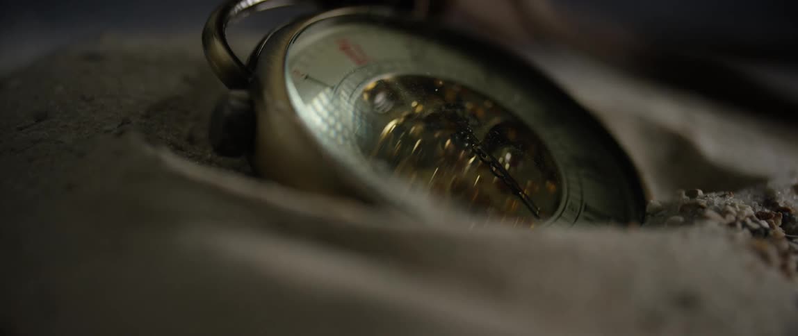 Light reflects on the face of a working pocket watch buried in sand